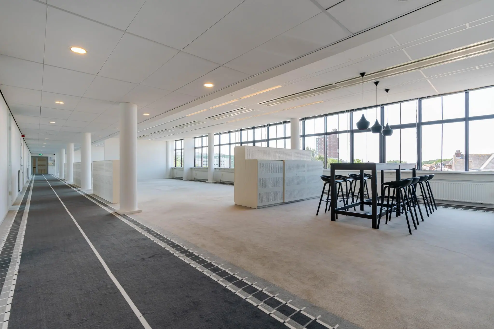 Moderne, lichte kantooretage aan de Van Alkemadelaan met open werkruimte, hoge ramen en een zitgedeelte met hoge tafel en krukken.